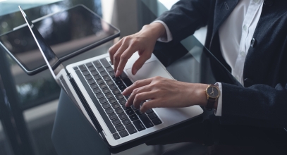 Businesswoman working on laptop computer with digital tablet on office table, close up. Business woman typing, searching the information, surfing the internet via laptop, online working at office, business technology